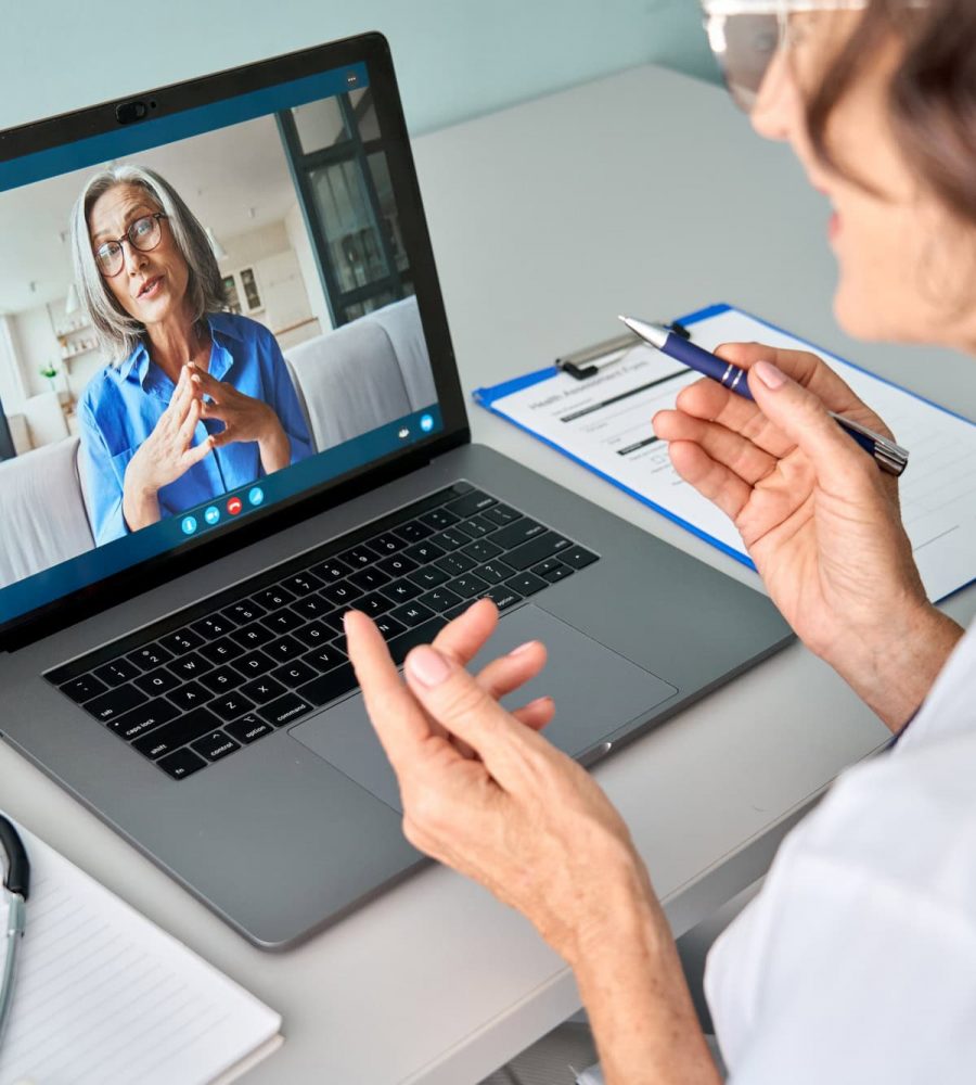Female doctor consulting older senior patient during virtual video call visit.